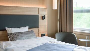 Une chambre d’hôtel avec un lit, une chaise, une petite table et une fenêtre avec des rideaux.