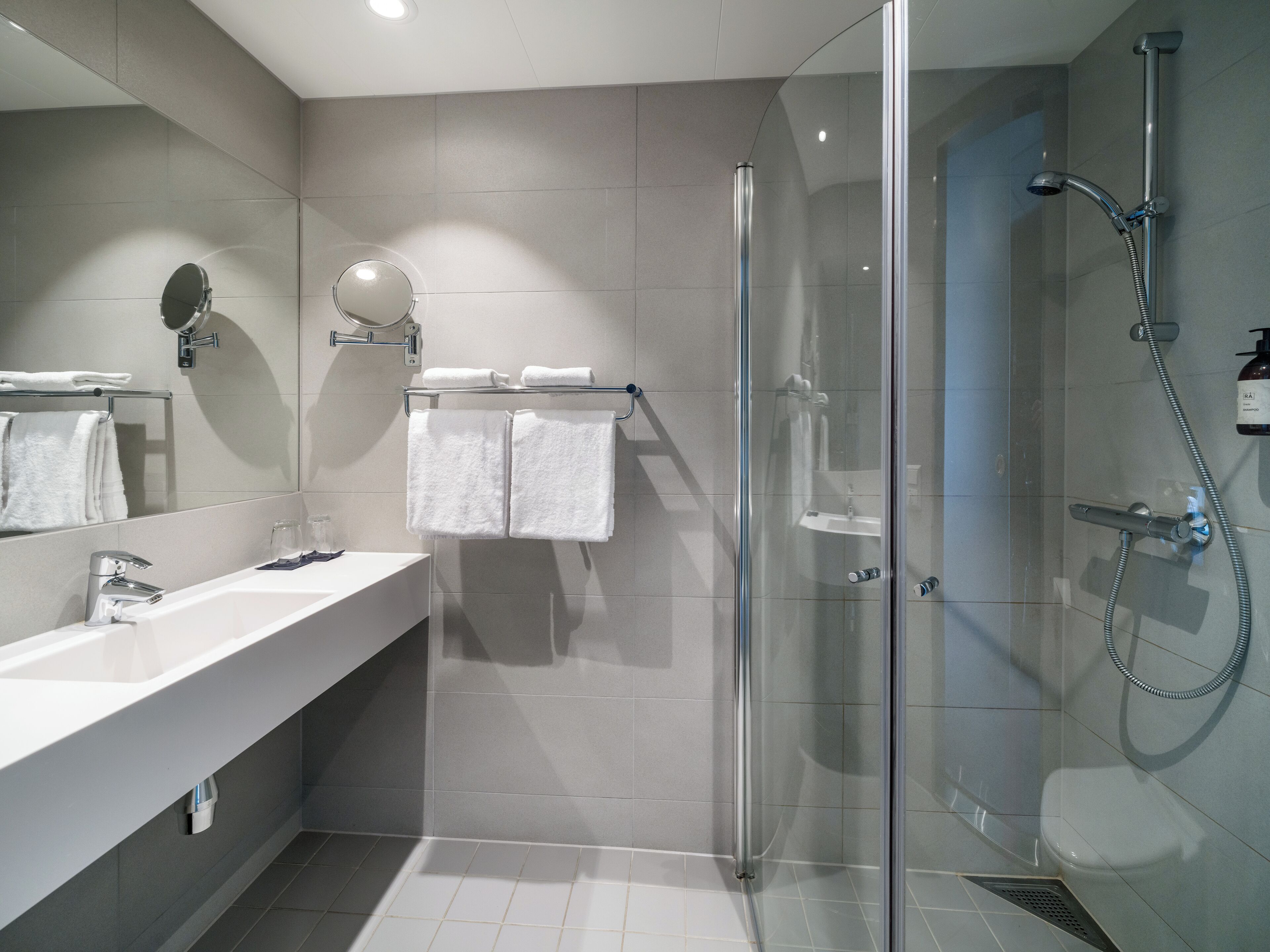 A modern bathroom with a glass-enclosed shower, a white sink with a mirror, and two towels hanging on a rack.
