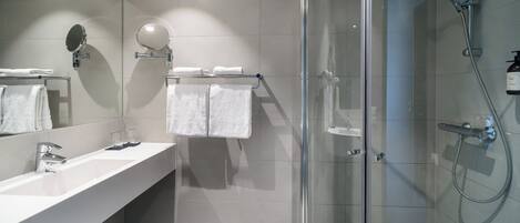 A modern bathroom with a glass-enclosed shower, a white sink with a mirror, and two towels hanging on a rack.