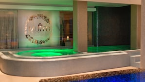 Un moderno espacio de spa con una bañera de hidromasaje, una pared decorativa con motivos florales y un separador de vidrio.