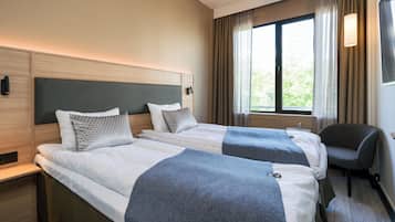 A hotel room with two beds, a desk, a chair, and a window with curtains.
