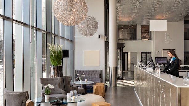 Un moderno hall de hotel con mostrador de recepción, zona de estar y grandes ventanales.