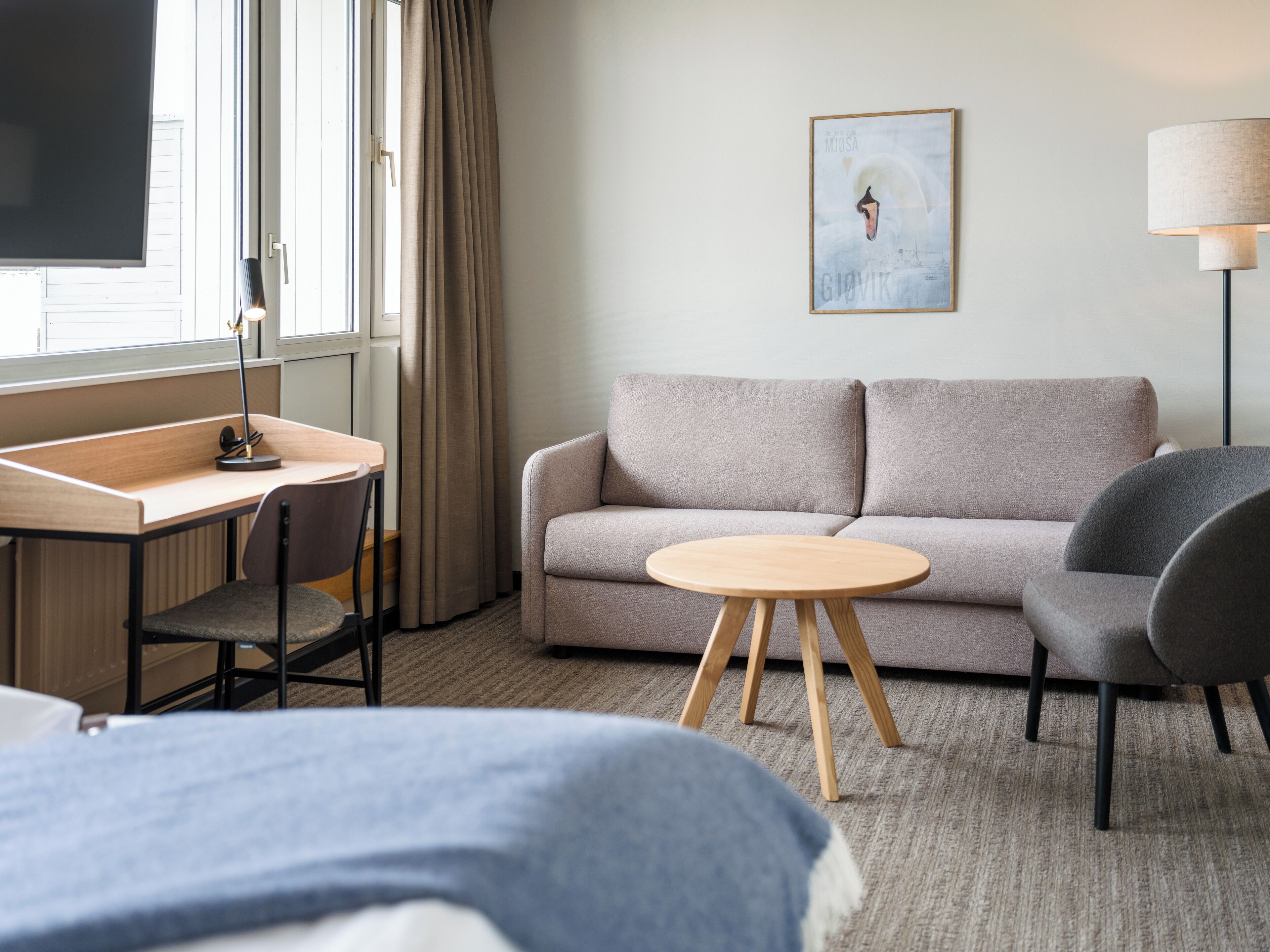 Ein modernes Hotelzimmer mit einer Couch, einem runden Tisch, einem Schreibtisch mit Stuhl und einer Lampe.