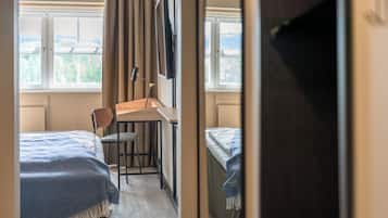 A room with two beds, a desk, and a chair. There is a window with a view of greenery.