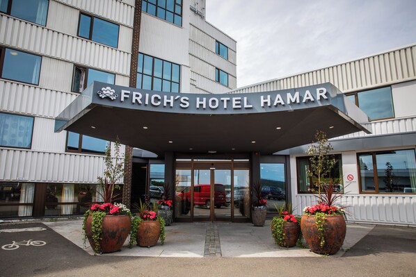 Frich's Hotel Hamar with a modern entrance, large potted plants, and a clear view of the parking area.