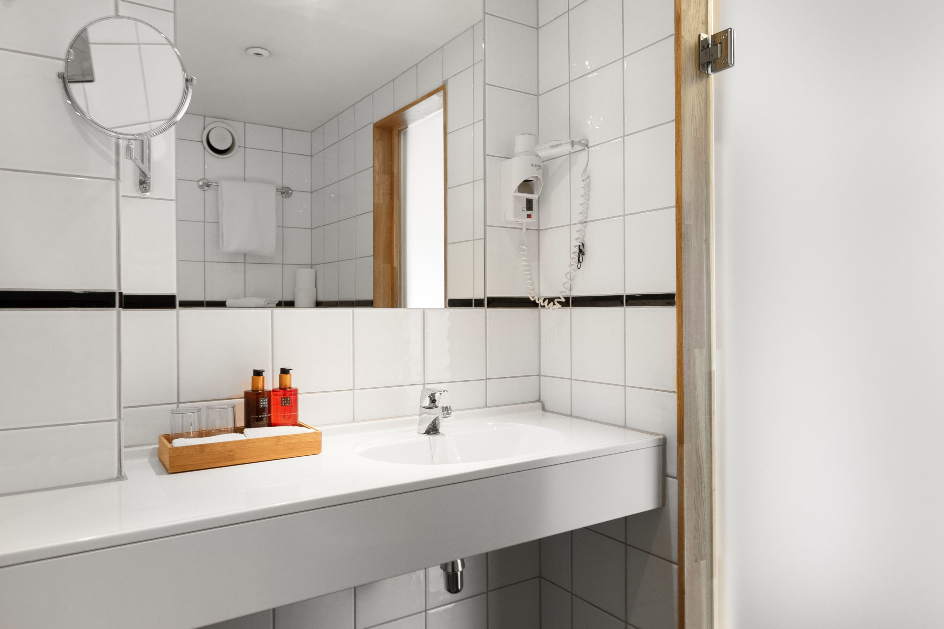 A modern bathroom with a white sink, a mirror, a towel rack, and a hairdryer.