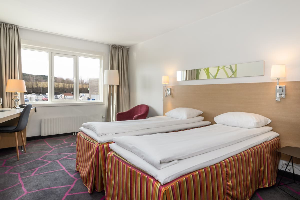 A hotel room with two beds, a desk, a chair, and a window with a view of the outside.