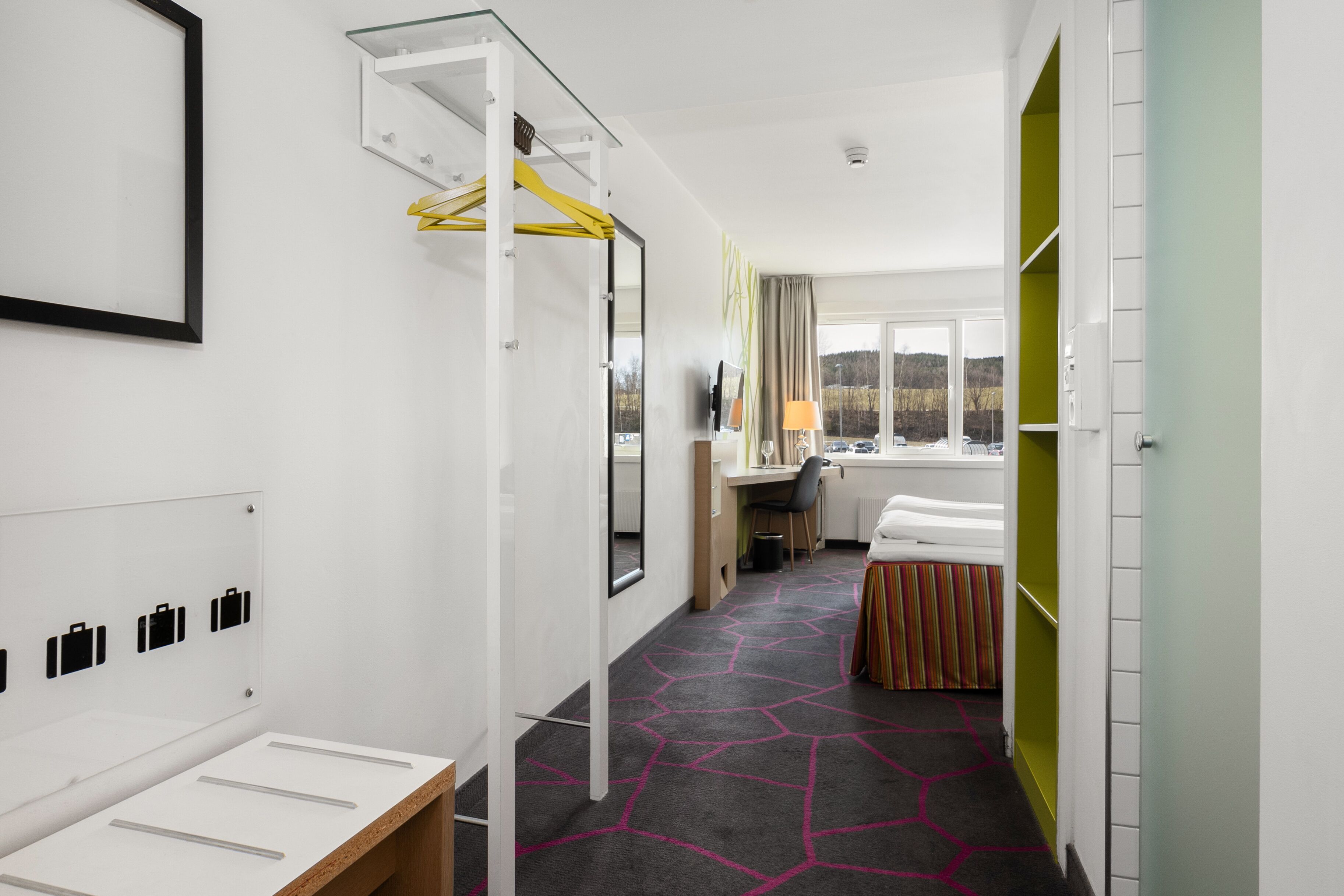 Camera d'albergo moderna con un letto, una scrivania, una sedia, uno specchio e una finestra con vista.