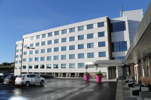 A modern hotel with a flat facade, multiple windows, and a parking lot with cars.
