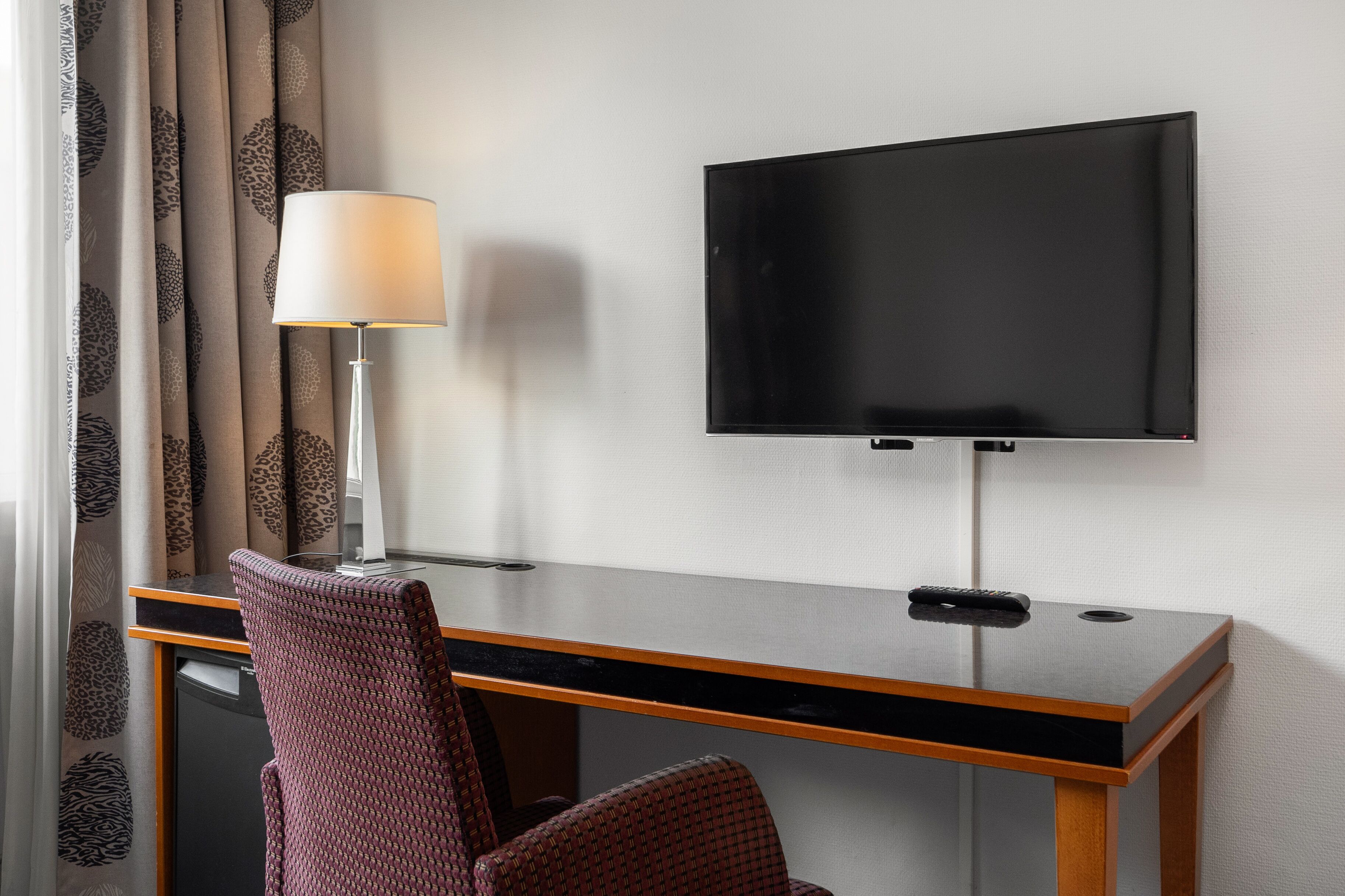Une chambre d’hôtel équipée d’un bureau, d’une télévision, d’une lampe et d’une chaise.