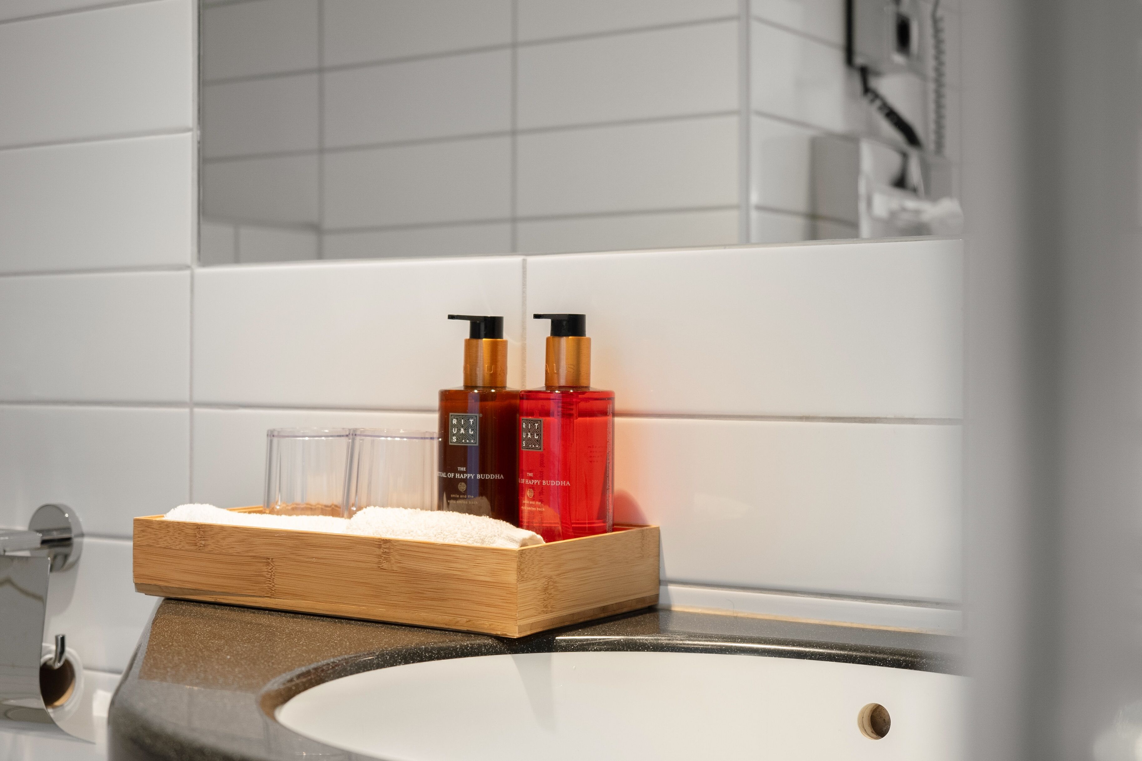 A bathroom with a wooden tray holding toiletries, a sink, and a mirror.