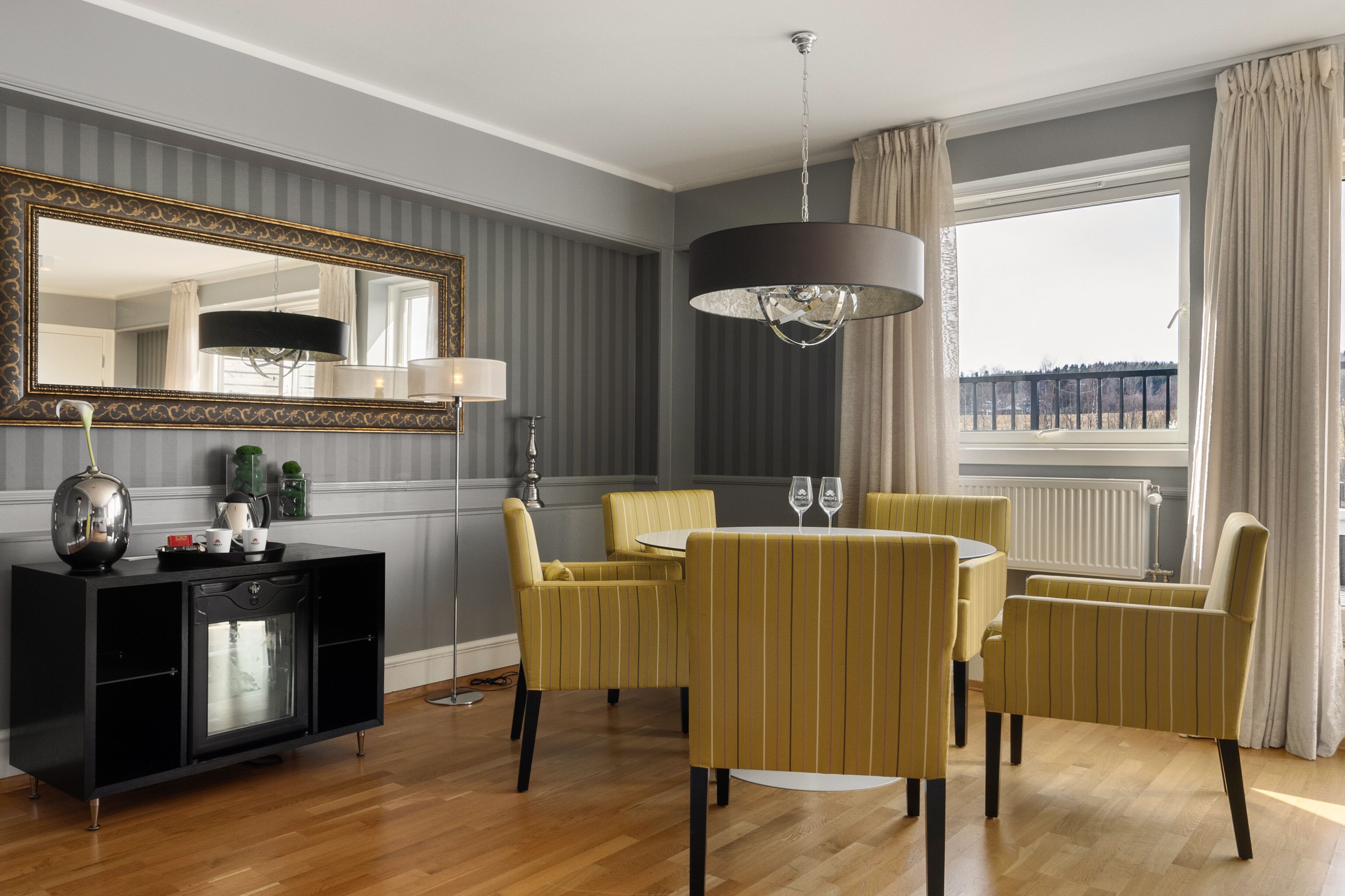 A room with a dining table, chairs, a black cabinet, a large mirror, and a window with curtains.