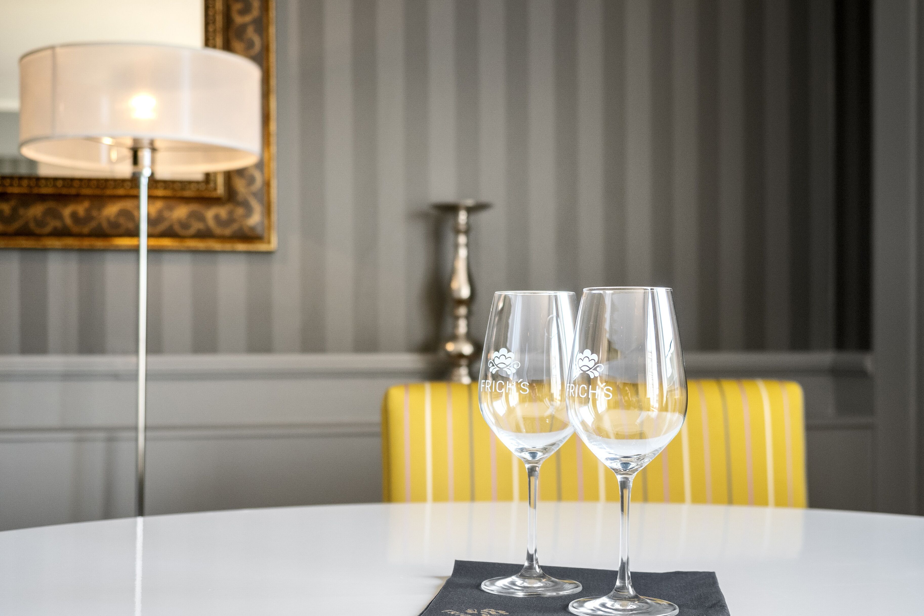 Two empty wine glasses on a white table with a lamp in the background.