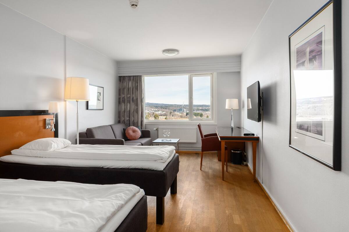 A hotel room with two beds, a desk, a chair, a TV, and a window with a city view.