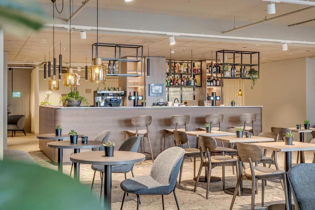 Een modern café met ronde tafels, stoelen en een bar voorzien van flessen en glazen.