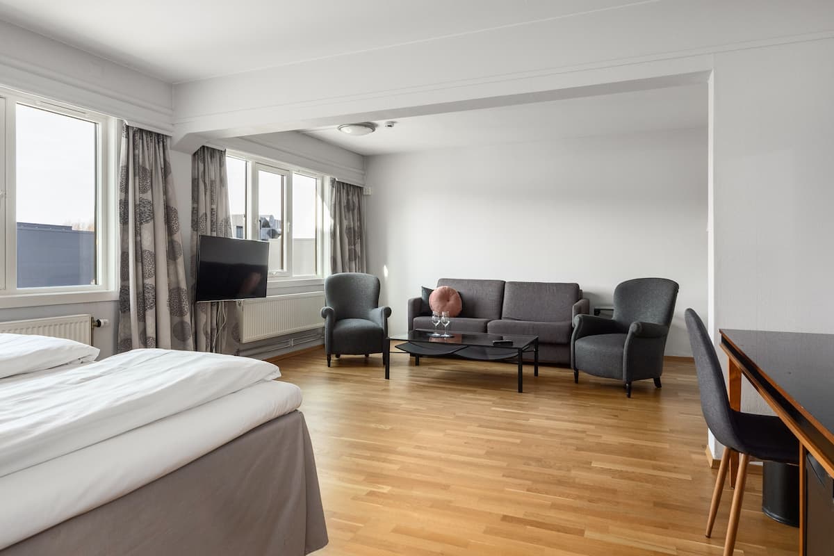 A modern hotel room with a bed, a sofa, a coffee table, and a TV.
