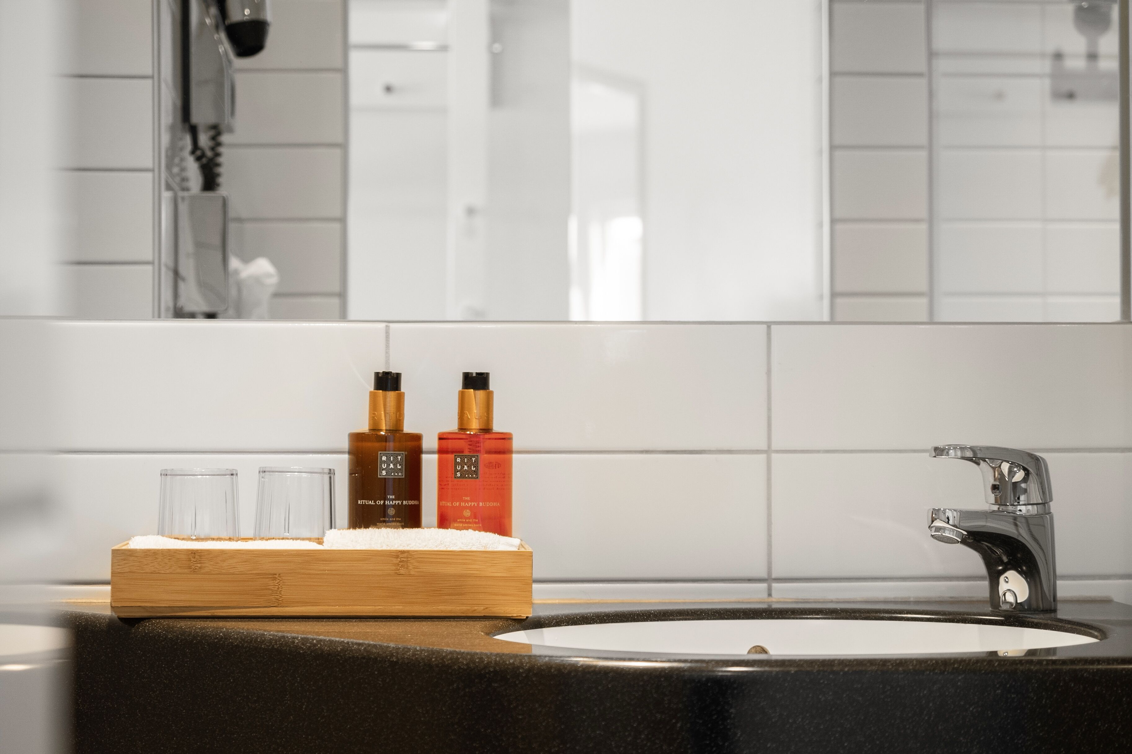 A bathroom with a black countertop, a white sink, and two bottles of lotion.