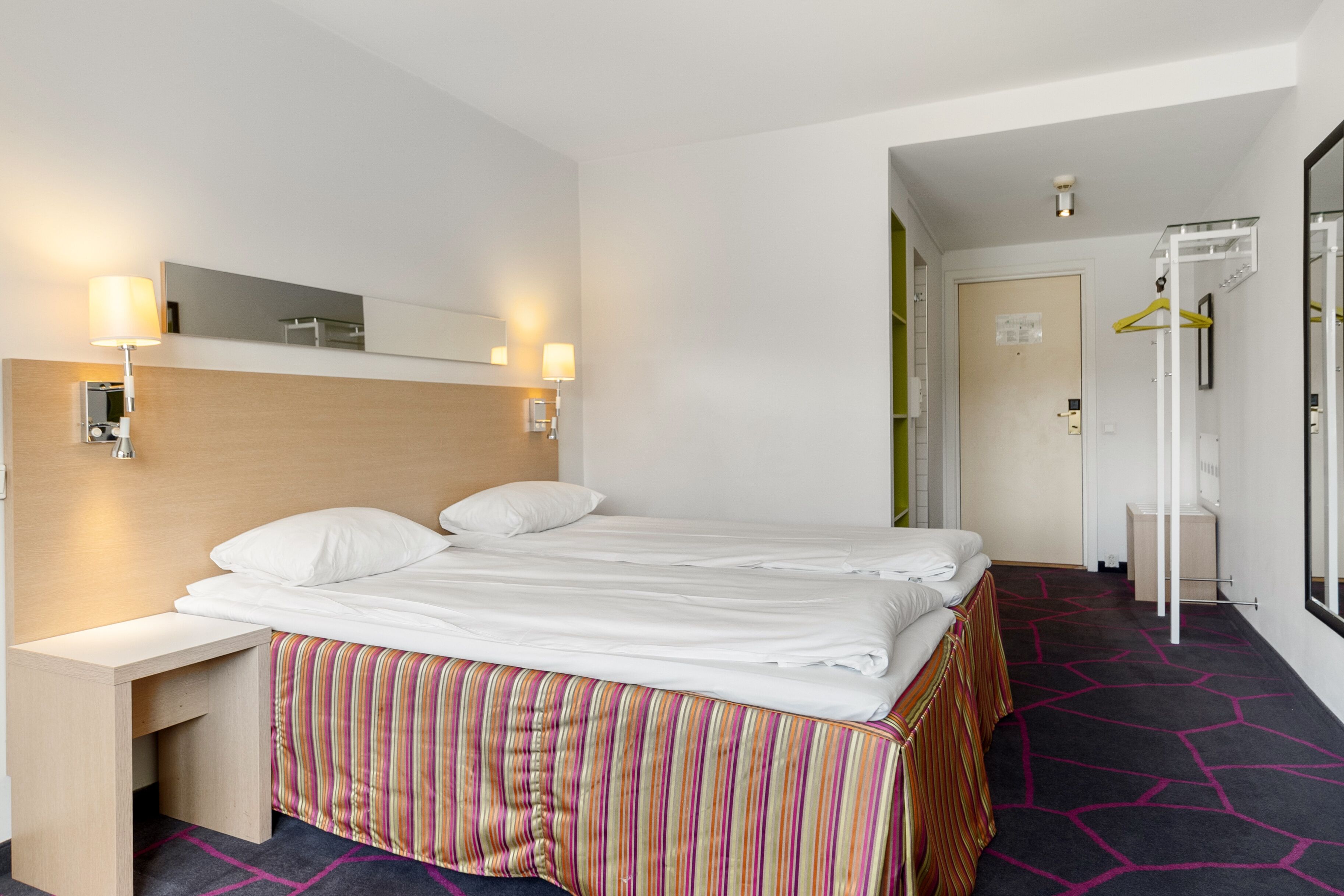 A hotel room with a bed, bedside tables, a mirror, and a wardrobe.