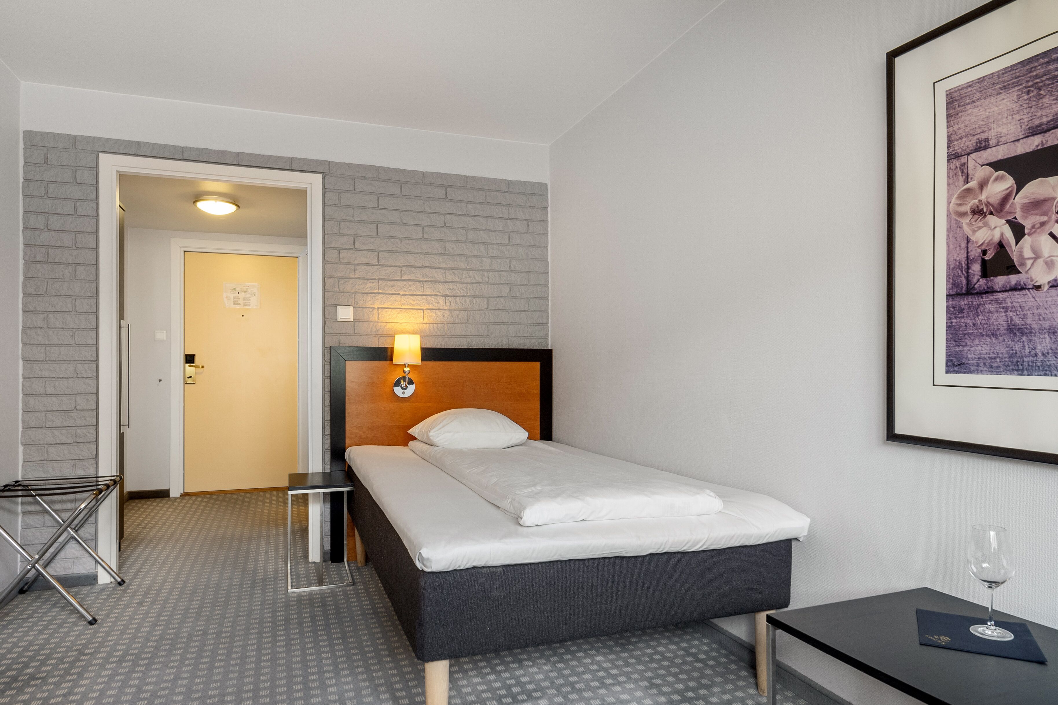 Une chambre d’h ôtel avec un lit, une table de chevet, un tableau encadré au mur et une porte donnant sur une autre pièce.
