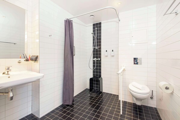 A bathroom with a white sink, a toilet, a shower with a black floor, and a grey shower curtain. - Scandic Hammerfest (Hammerfest)