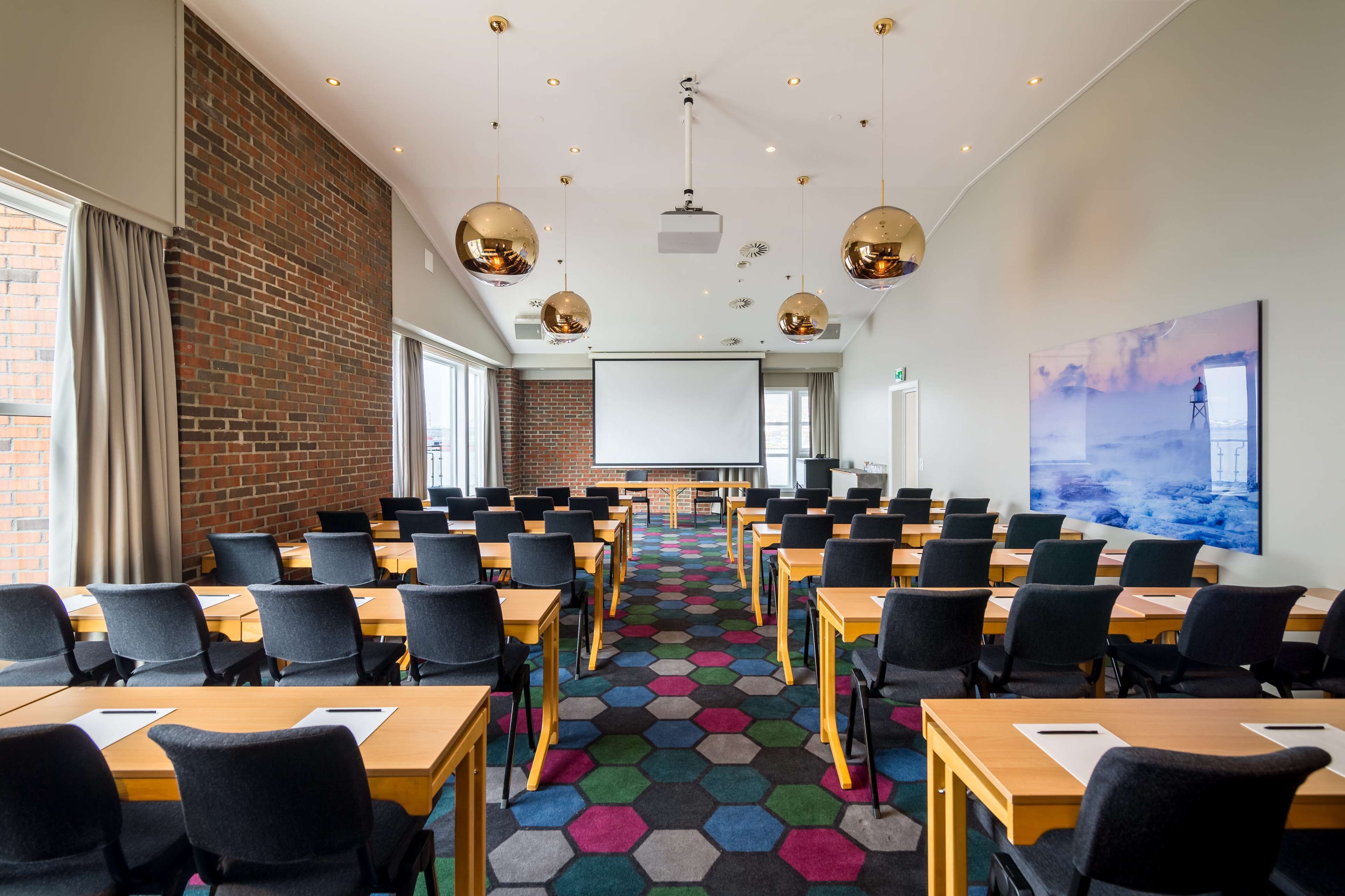 A conference room with hexagonal patterned carpet, wooden tables, and black chairs.
