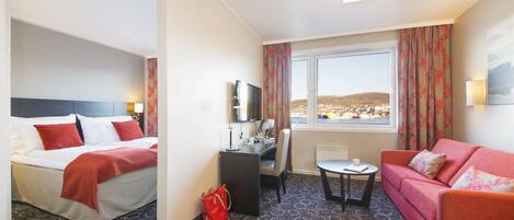 A hotel room with a bed, a desk, a sofa, a TV, and a window with a view.