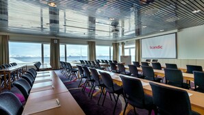 A conference room with a large screen displaying "Scandic," rows of tables and chairs, and a view of the ocean through large windows. - Scandic Hammerfest (Hammerfest)