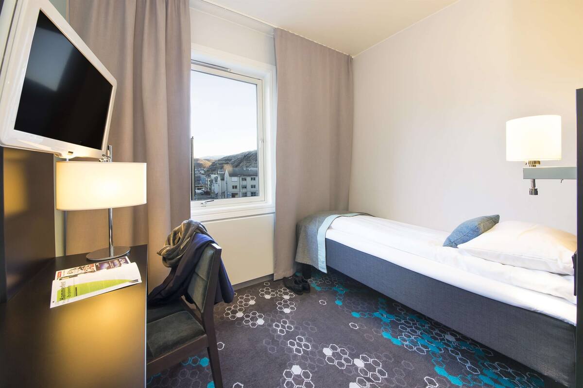Ein Hotelzimmer mit Bett, Schreibtisch, Fernseher, Fenster und Lampe.