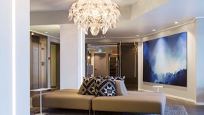 A modern lobby with a beige sofa, patterned pillows, a unique chandelier, and a large abstract painting on the wall. - Scandic Harstad (Harstad)