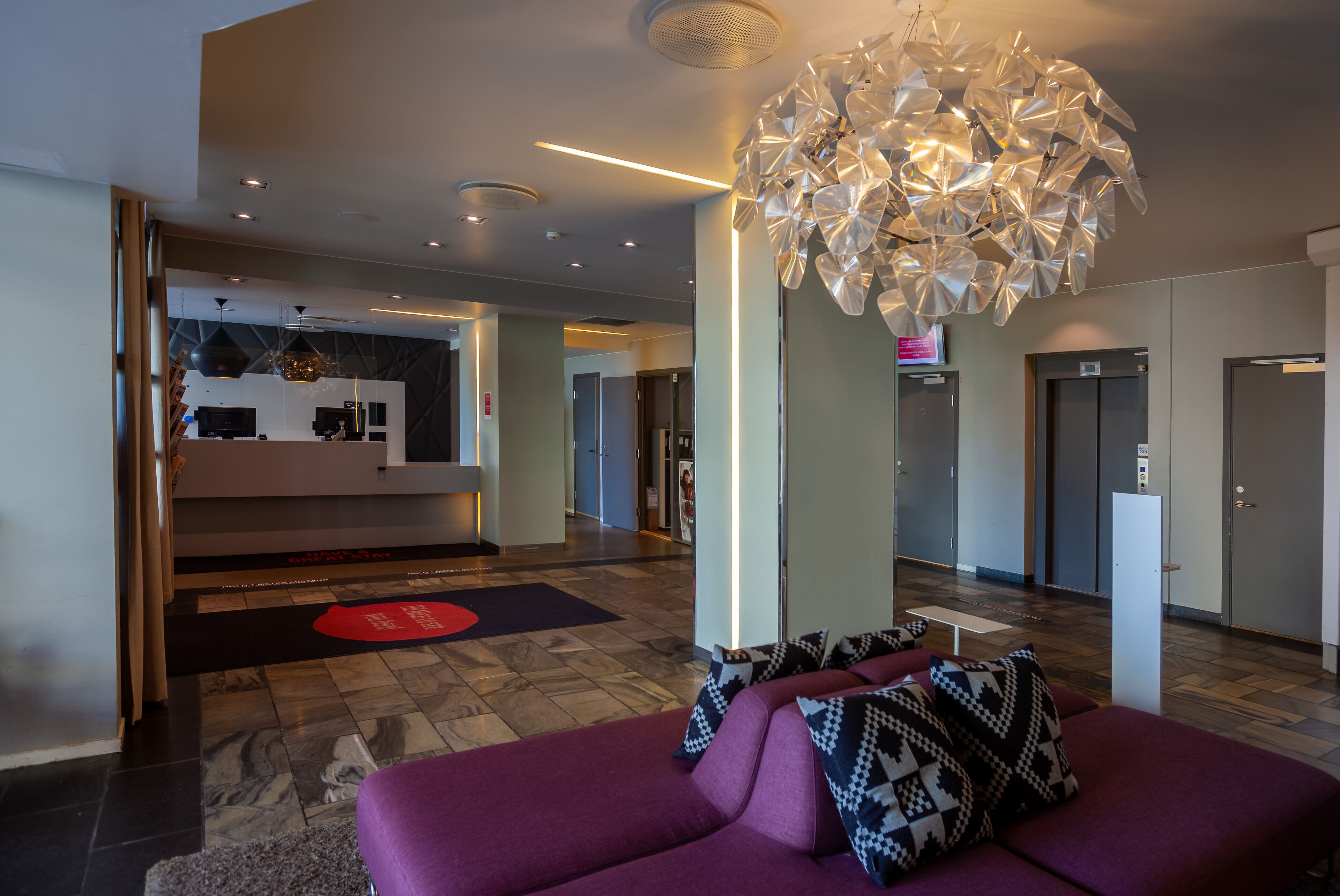 A modern lobby with a purple sofa, a unique chandelier, and a reception desk.