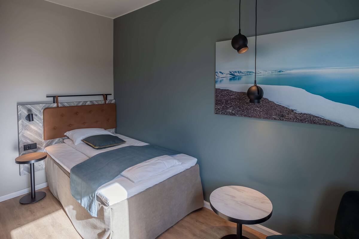 A modern bedroom with a bed, a round table, and a painting of a snowy landscape.