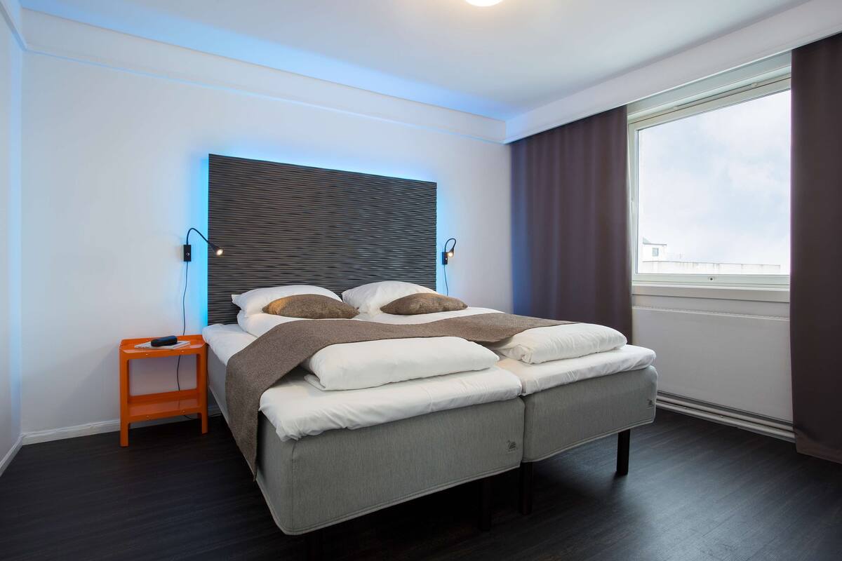 A modern bedroom with a bed, bedside table, and a large window.