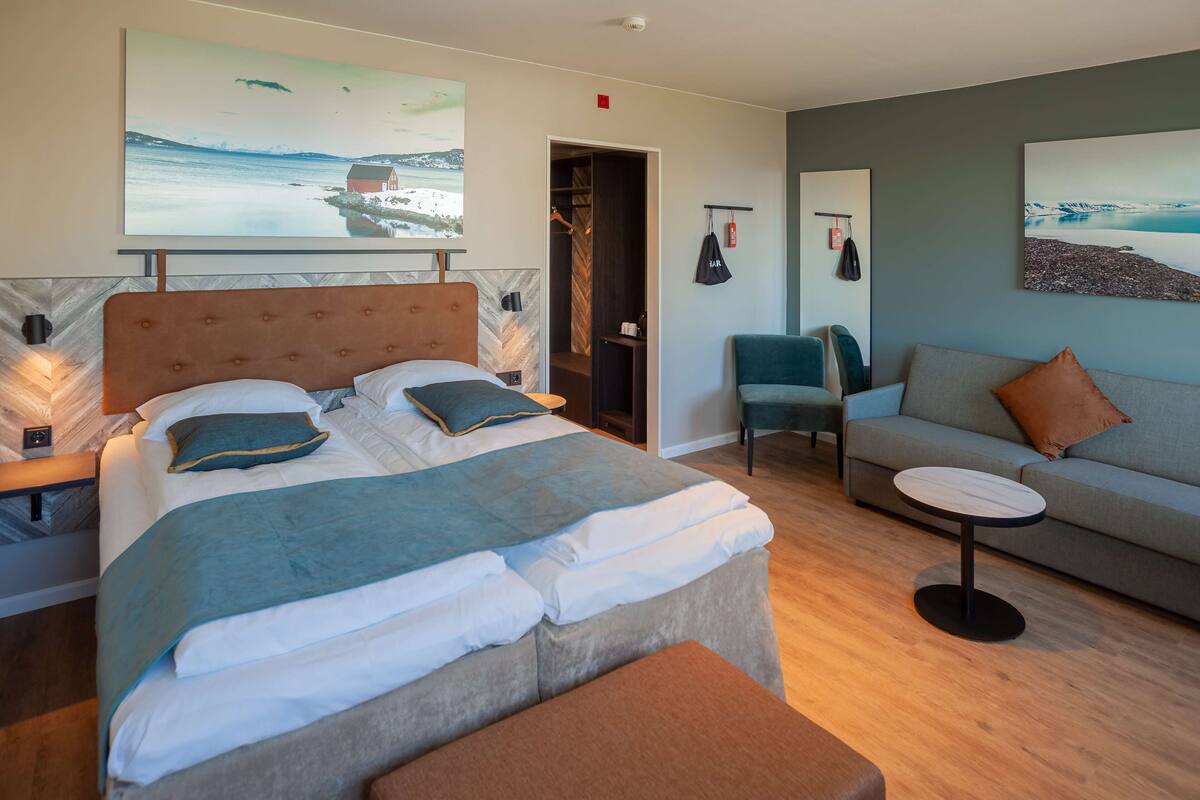 A modern hotel room with a large bed, a sofa, a small round table, and artwork on the walls.