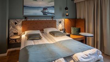 Habitación de hotel moderna con una cama grande, una mesita de noche pequeña, una mesita auxiliar y un proyector mural que muestra una imagen panorámica.