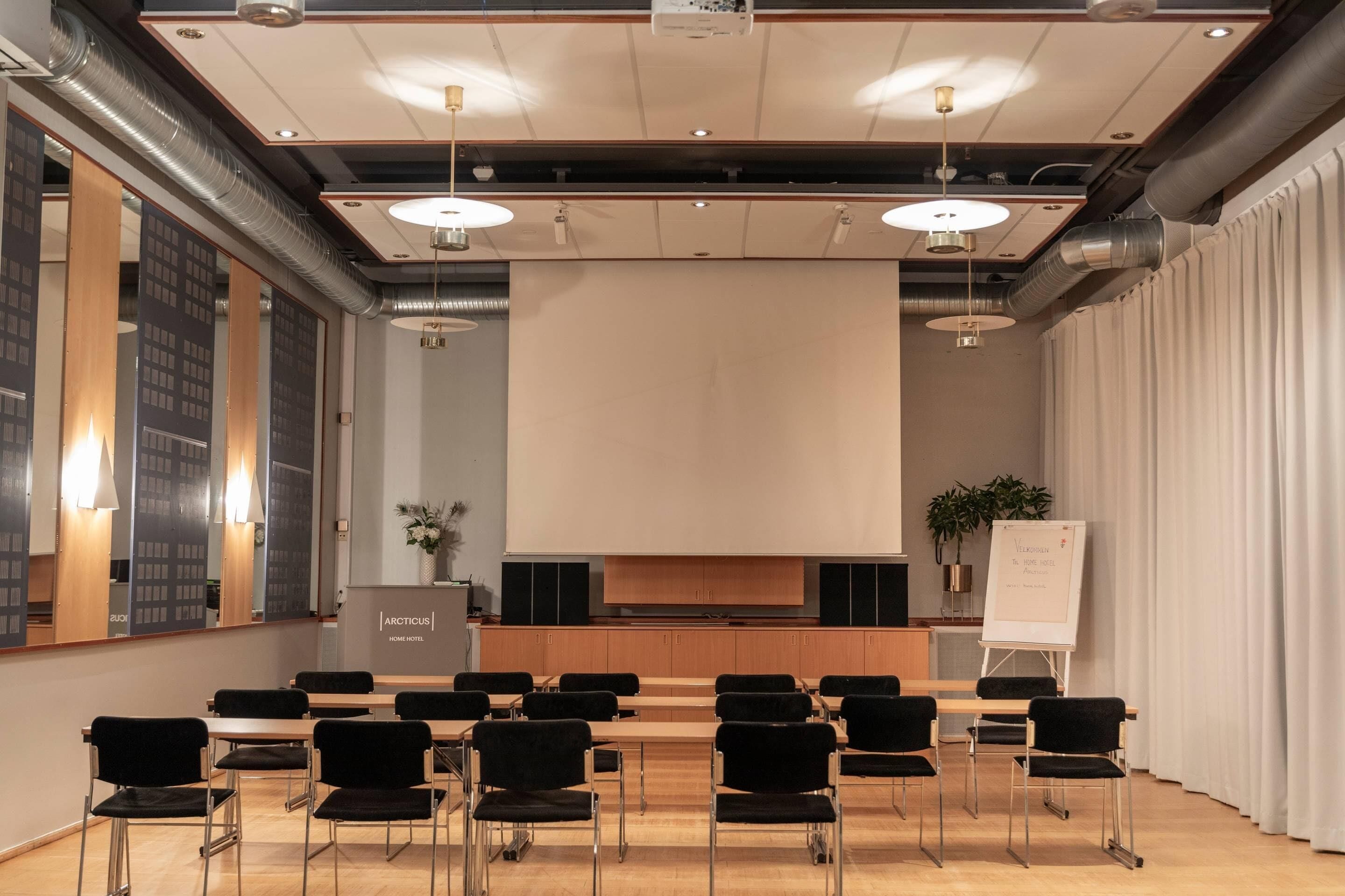 A conference room with a large screen, black chairs, wooden tables, and a whiteboard.