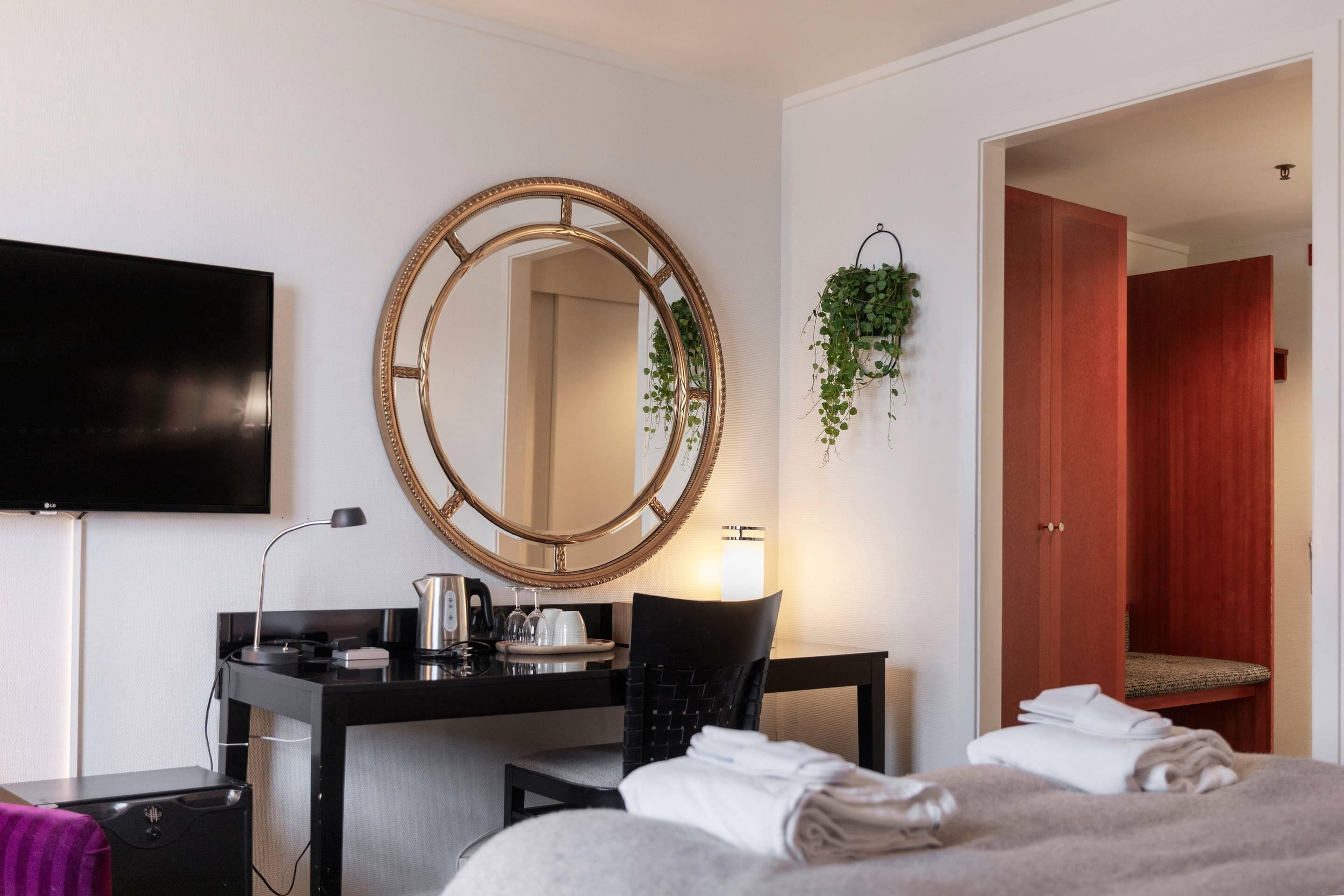 Una camera d'albergo con un letto, una scrivania con lampada, una televisione, uno specchio e un armadio rosso.