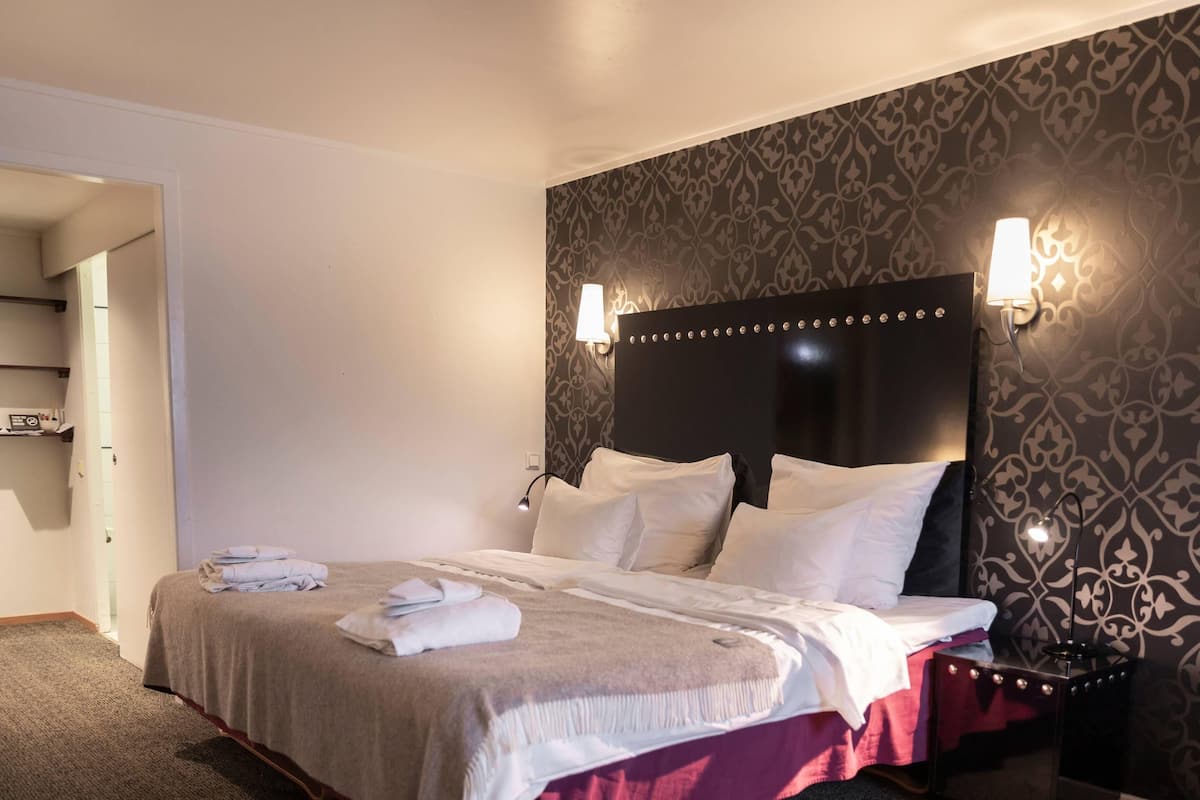 Una cama bien hecha con ropa de cama blanca y roja, un cabecero con luces decorativas y un papel tapiz estampado en la pared.