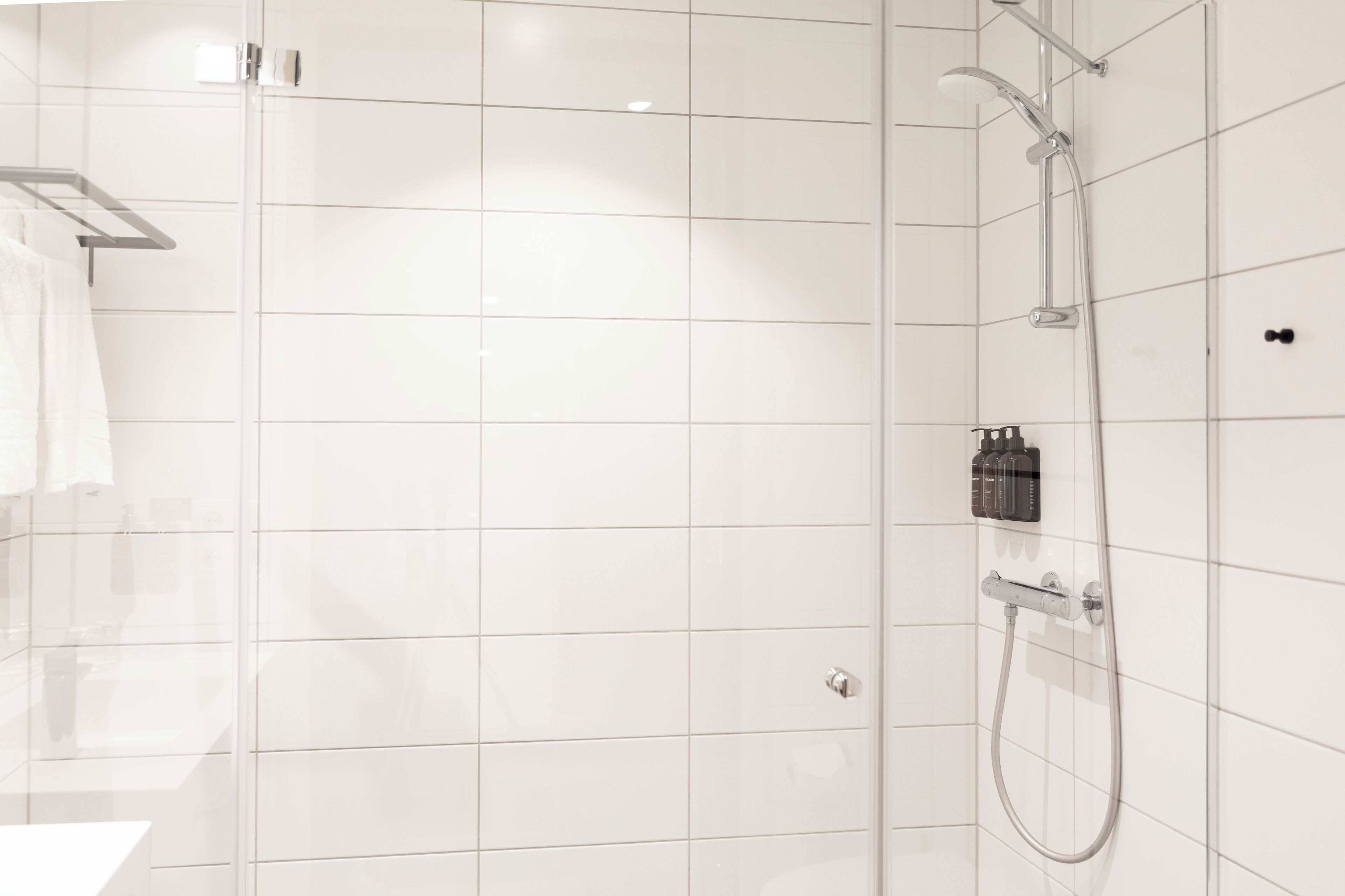 A modern bathroom with white tiled walls, a glass shower enclosure, and a towel rack.