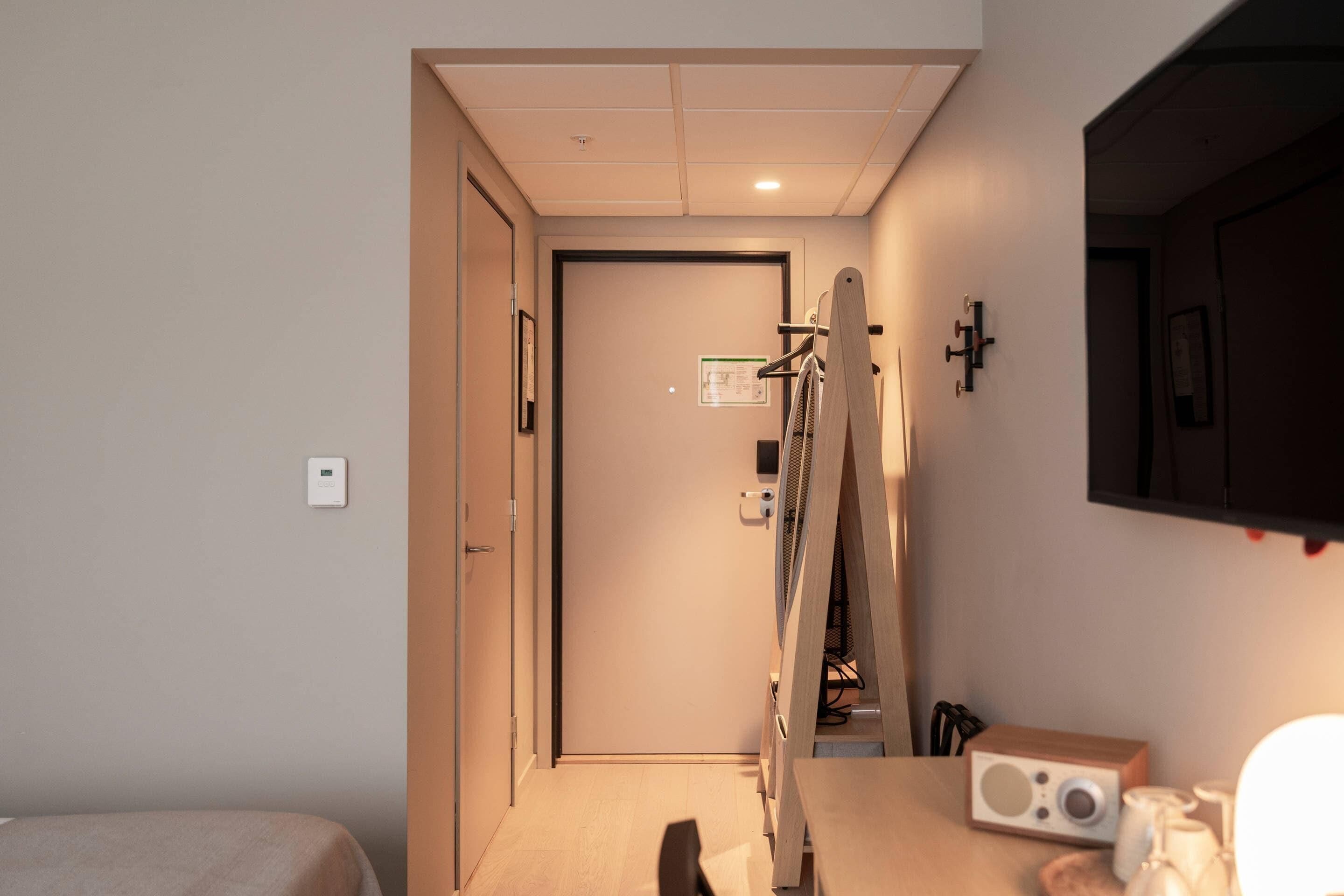 Een hotelkamer met een bed, een bureau, een stoel, een radio en een deur naar een andere kamer.