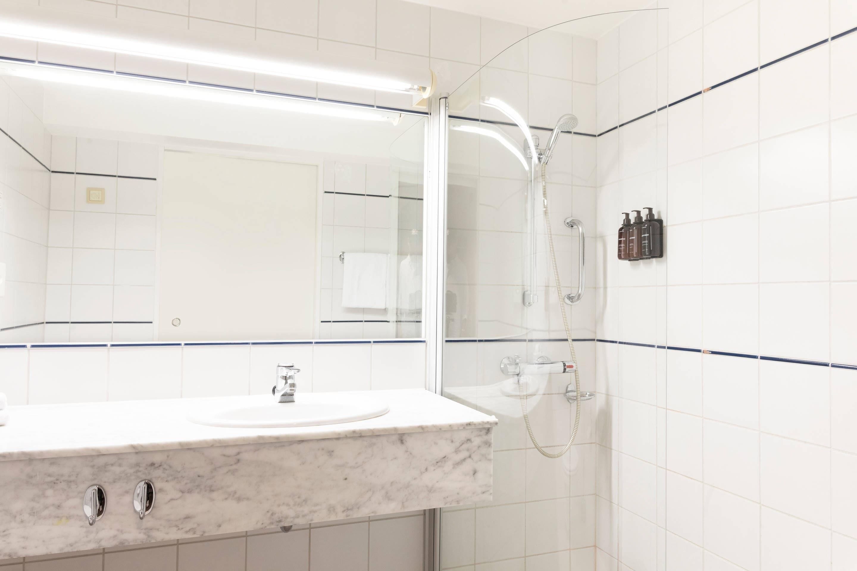 A bathroom with a marble sink, a glass-enclosed shower, and white tiled walls.