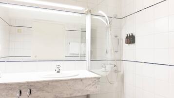 A bathroom with a marble sink, a glass-enclosed shower, and white tiled walls.