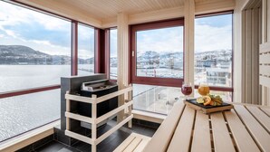 Un balcón con una mesa de madera, una parrilla y vistas a un lago y edificios.