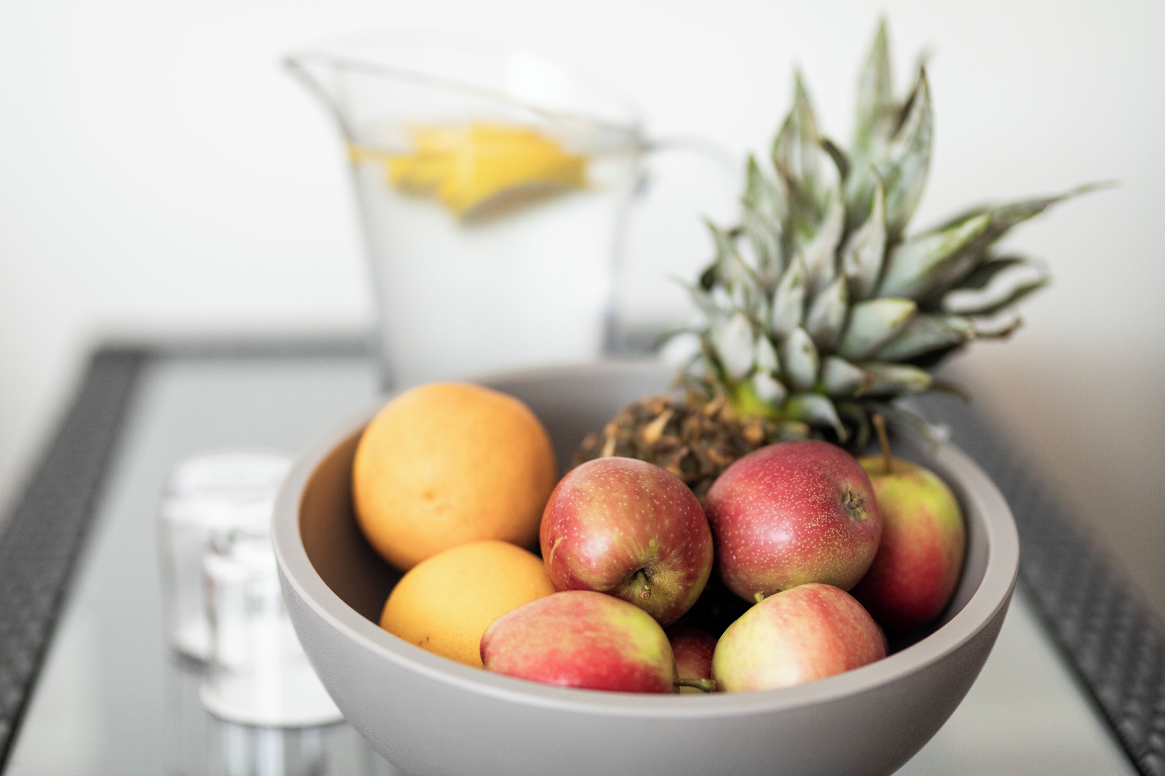 A bowl of fruit including apples, a pineapple, and an orange on a table.