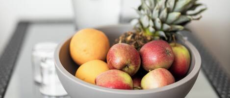 A bowl of fruit including apples, a pineapple, and an orange on a table.