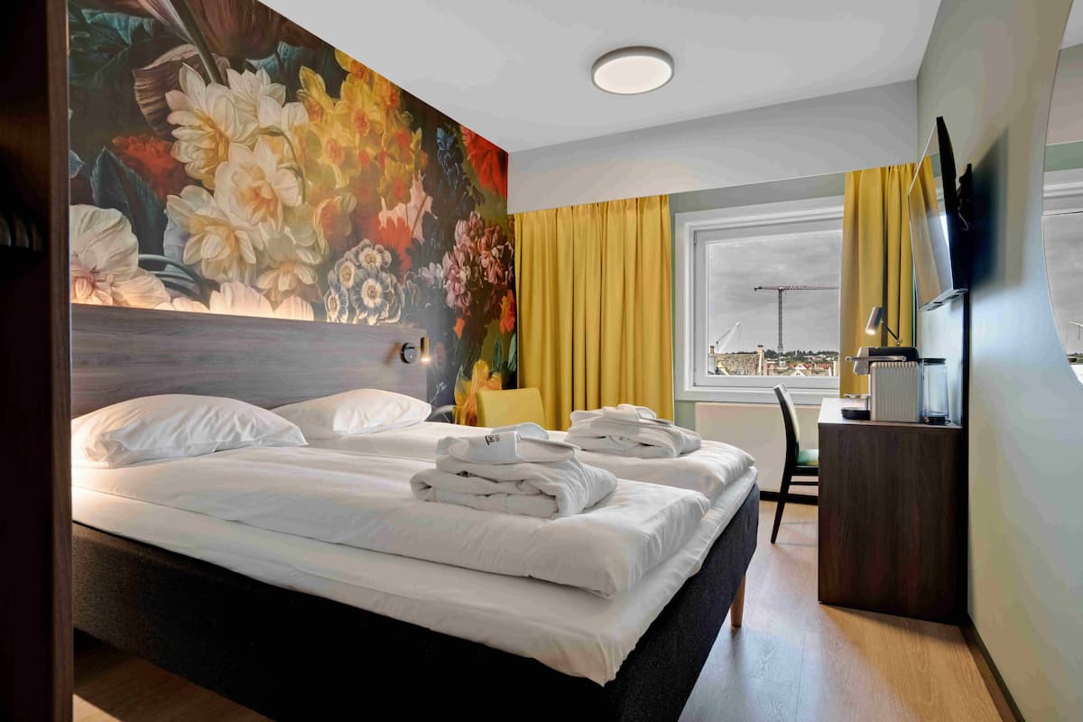 A hotel room with a large bed, a desk, a chair, and a window with curtains.
