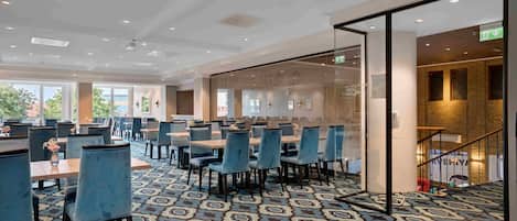 Un amplio vestíbulo de hotel con alfombra estampada, mobiliario moderno y ventanas grandes que ofrecen vistas al exterior.
