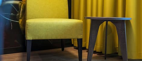 Un sillón amarillo y una mesita en una habitación con cortina amarilla y un cuadro de fondo.