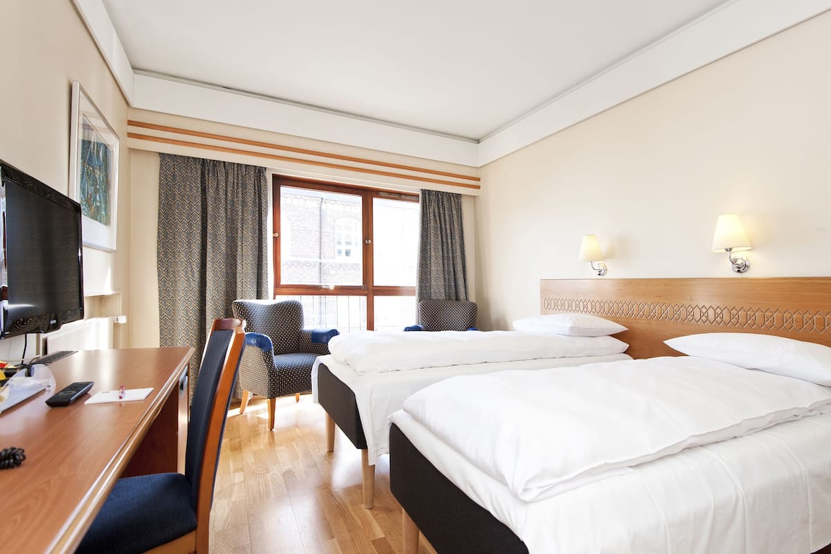 A hotel room with two beds, a desk with a computer, a chair, and a TV.