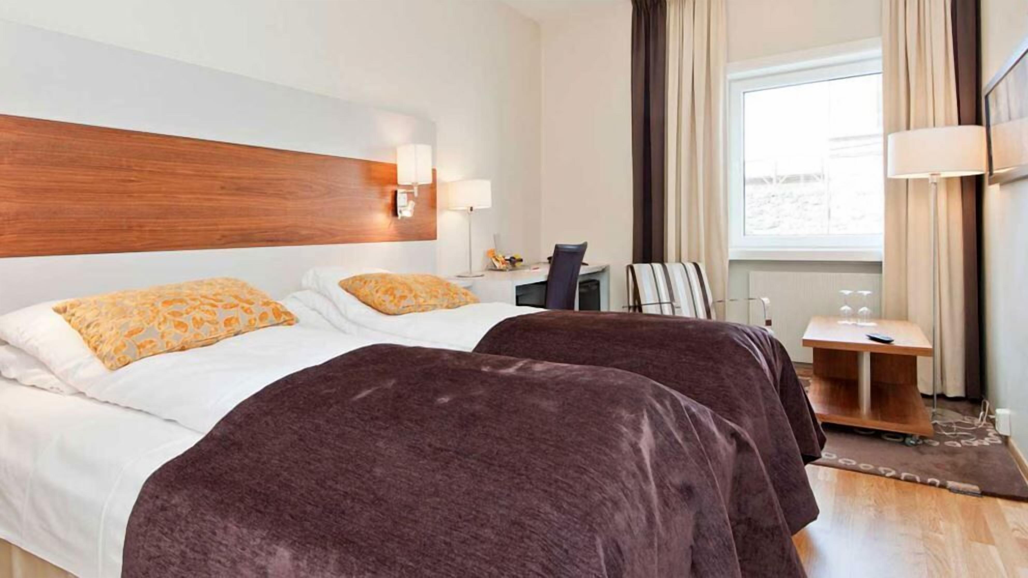 Une chambre d’hôtel avec deux lits, un bureau, une chaise, une lampe et une vue sur l’extérieur.