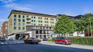 A multi-story hotel with a green facade, a parking lot, and a red car parked on the street. - Thon Hotel Saga (Haugesund)
